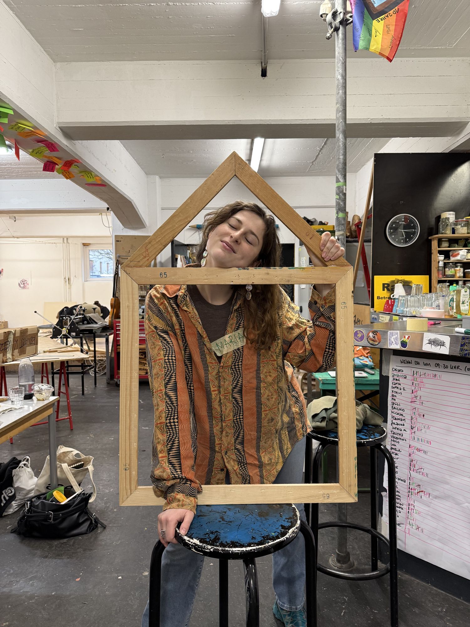 Maria holding a wooden frame shaped like a house in front of her face